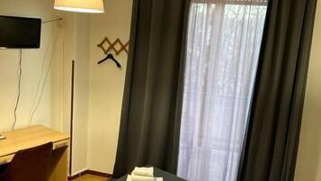 Et hotelværelse med seng, skrivebord, stol, fjernsyn og et vindue med gardiner.