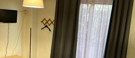 A hotel room with a bed, a desk, a chair, a TV, and a window with curtains.