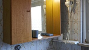 A bathroom with a wooden vanity, a mirror, a hairdryer, and a window with patterned tiles. - Hotel Amica (Salsomaggiore Terme)
