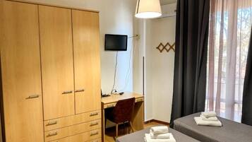Ein Zimmer mit Holzschrank, Schreibtisch mit Stuhl, Bett mit gefaltetem Handtuch und Fernseher an der Wand.