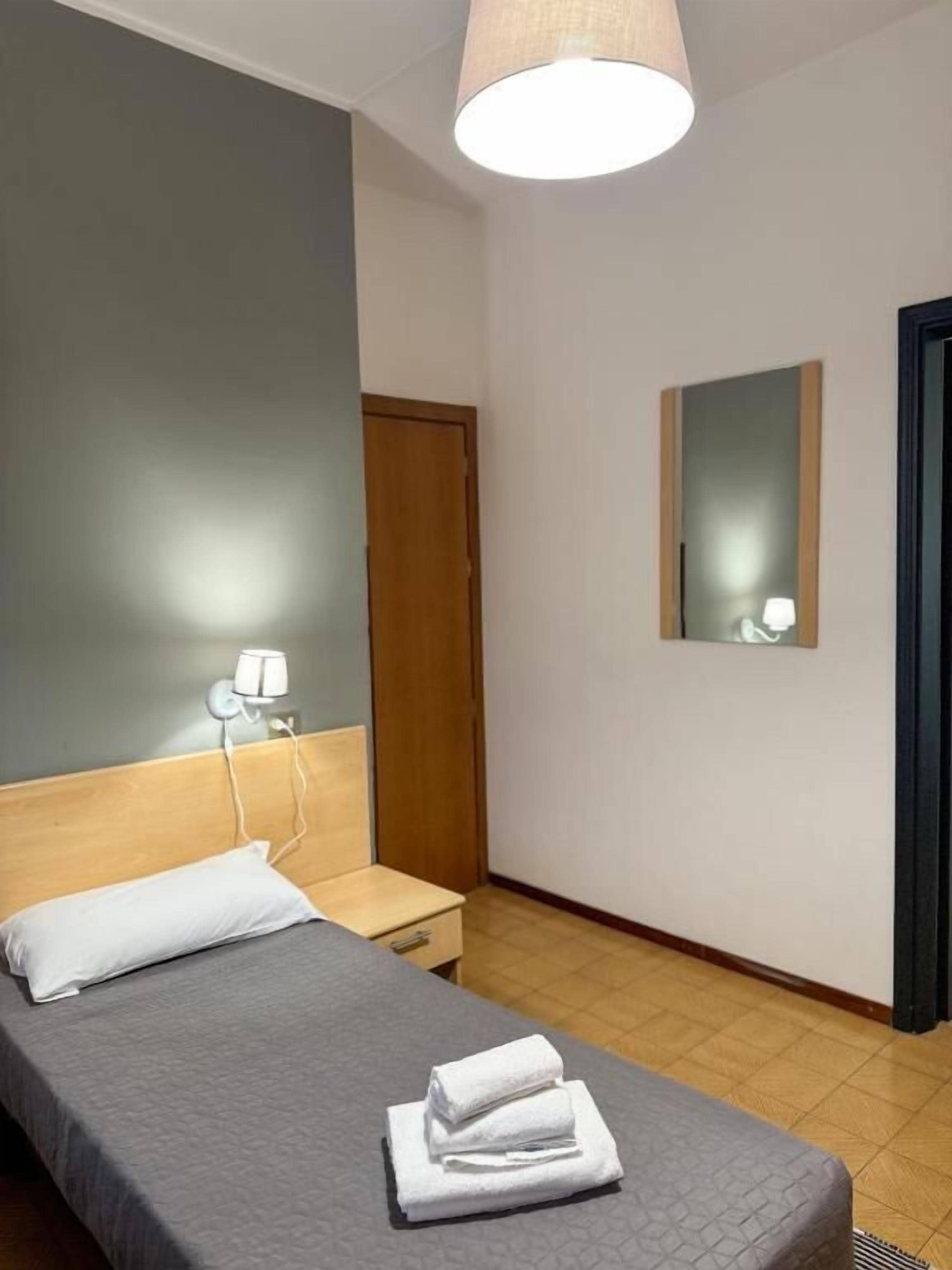 Una habitación de hotel con cama, mesita de noche, lámpara, espejo y puerta.