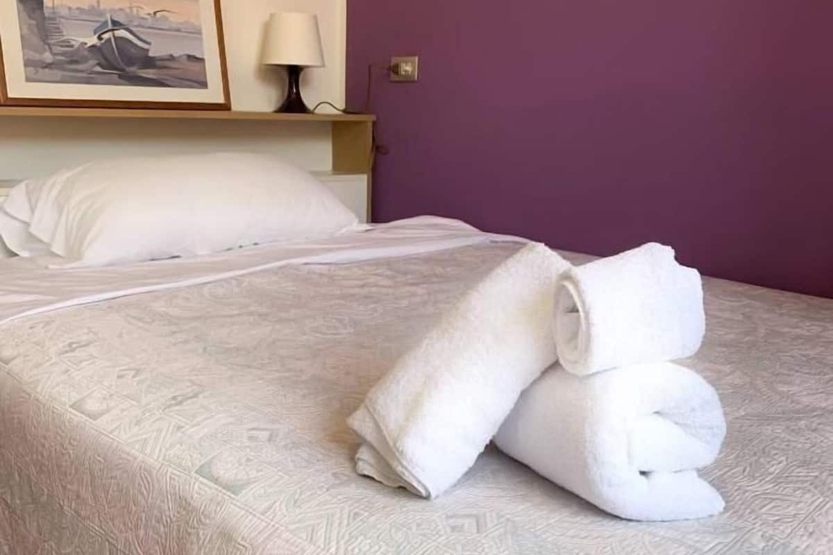 Een keurig opgemaakt bed met een bedsprei met dessin, een opgerolde witte handdoek en een ingelijst foto op het nachtkastje.