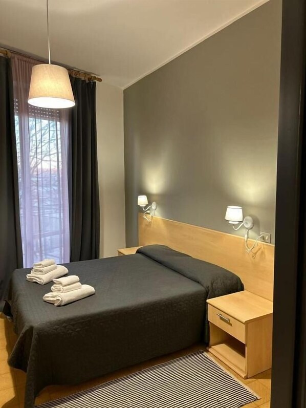 Una habitación de hotel moderna con una cama grande, mesitas de noche y vistas al exterior a través de la ventana.
