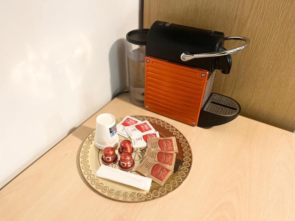 Une machine à café, un verre d’eau et un plateau contenant des sachets de café et une cuillère, le tout posé sur une table en bois.