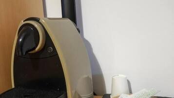 Una cafetera compacta con un panel de control, un pequeño plato con condimentos y una taza blanca sobre una mesa de madera.