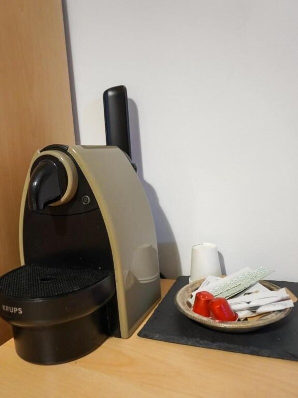A compact coffee machine with a control panel, a small plate with condiments, and a white mug on a wooden table. - Hotel Amica (Salsomaggiore Terme)