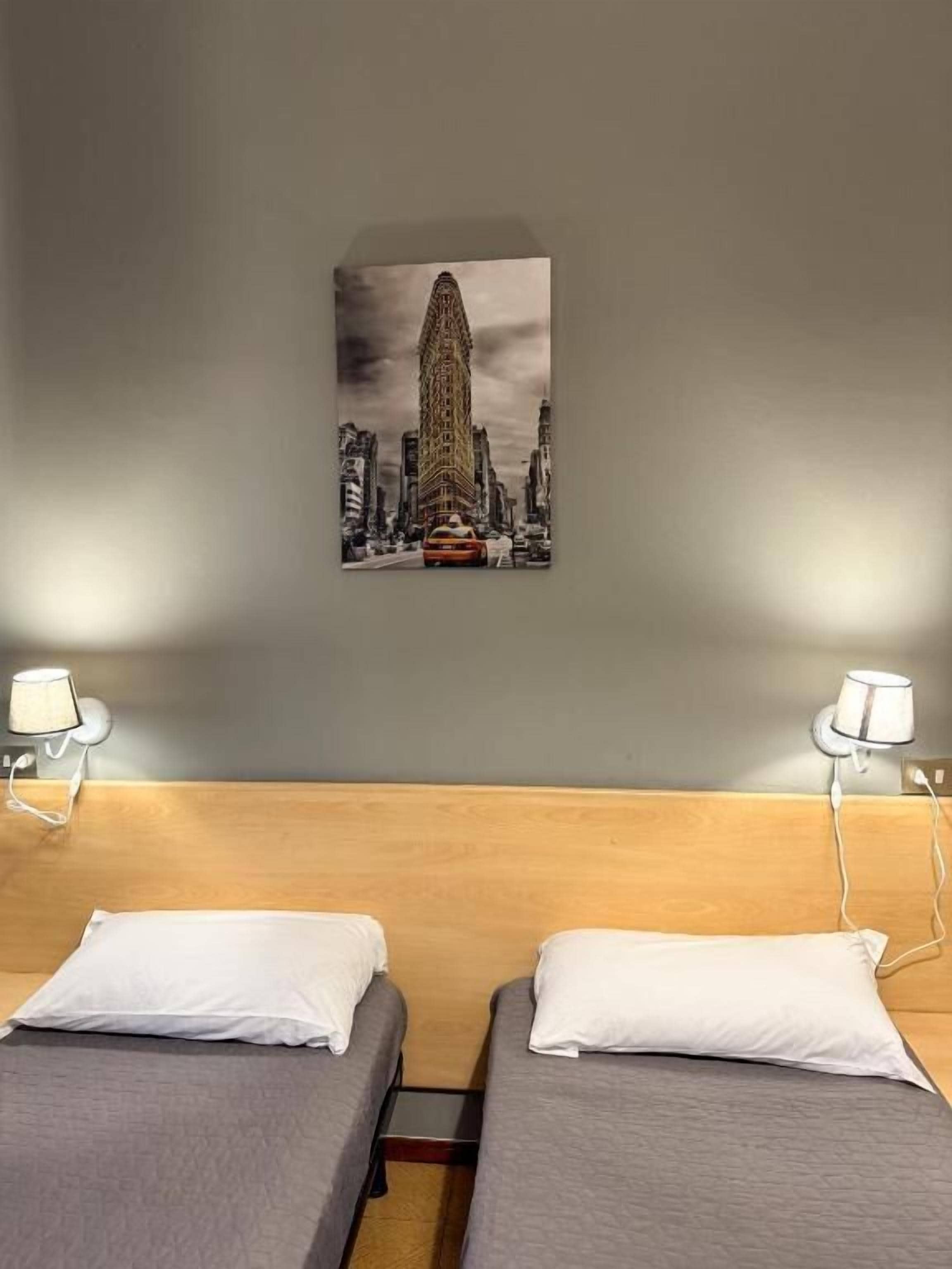A hotel room with two beds, a wooden headboard, and a cityscape painting on the wall.