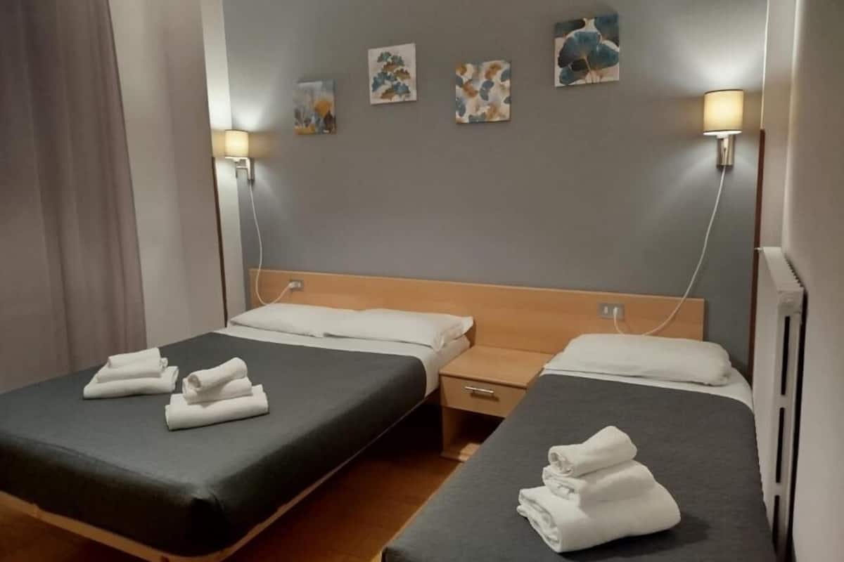 Een hotelkamer met twee bedden, elk voorzien van een keurig opgevouwen handdoek, een houten hoofdbord, nachtkastjes en wandlampen.