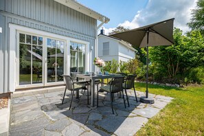 A patio with a table and chairs, a large umbrella, and a stone pathway leading to a house with a white exterior and large glass doors. - Modern living close to the beach for up to 6 people (Dierhagen)