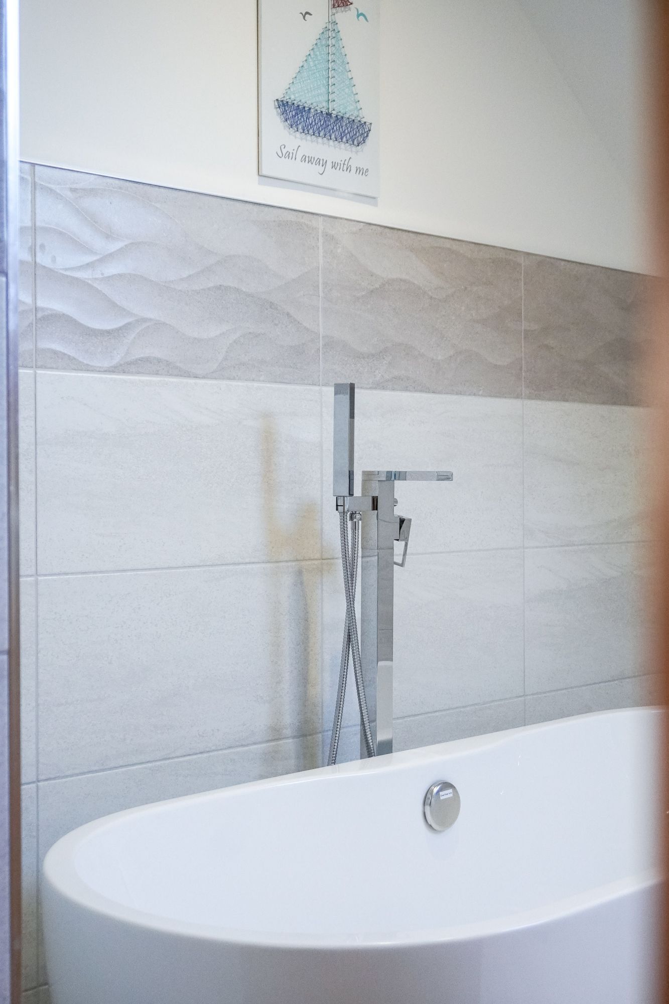 Un baño con una bañera blanca, ducha con cabezal de mano y un toallero de pared.