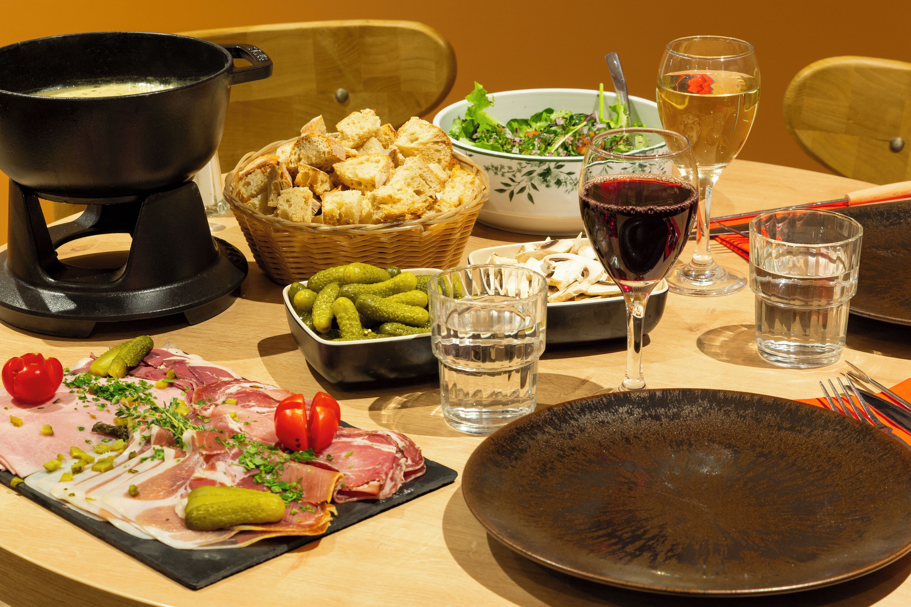 Ein Tisch reichhaltig gedeckt mit verschiedenen Speisen, darunter Fleisch, eingelegtes Gemüse und Brot, sowie Weingläsern und Wasser.