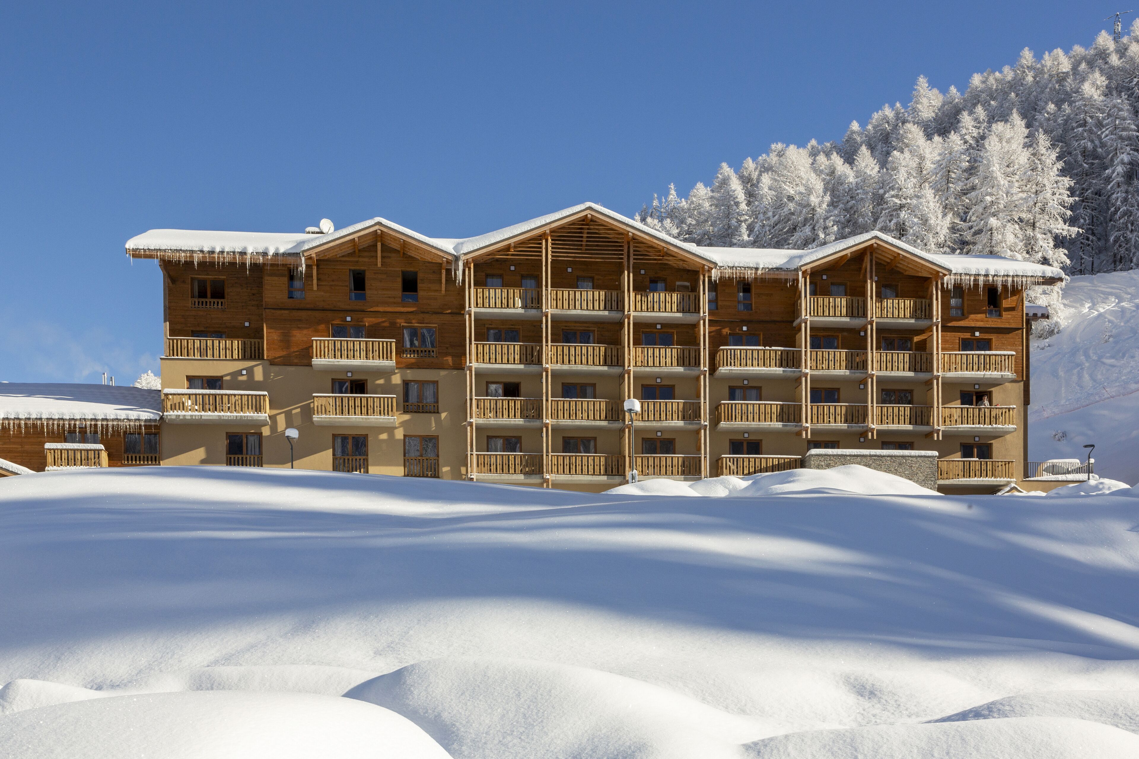 Un chalet en bois à plusieurs étages, doté de balcons et entouré d’arbres couverts de neige.