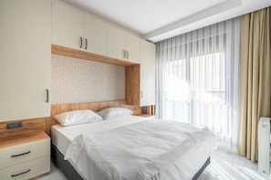 A modern bedroom with a large bed, wooden headboard, built-in wardrobe, and a window with sheer curtains. - Gokmen Suites (Antalya)