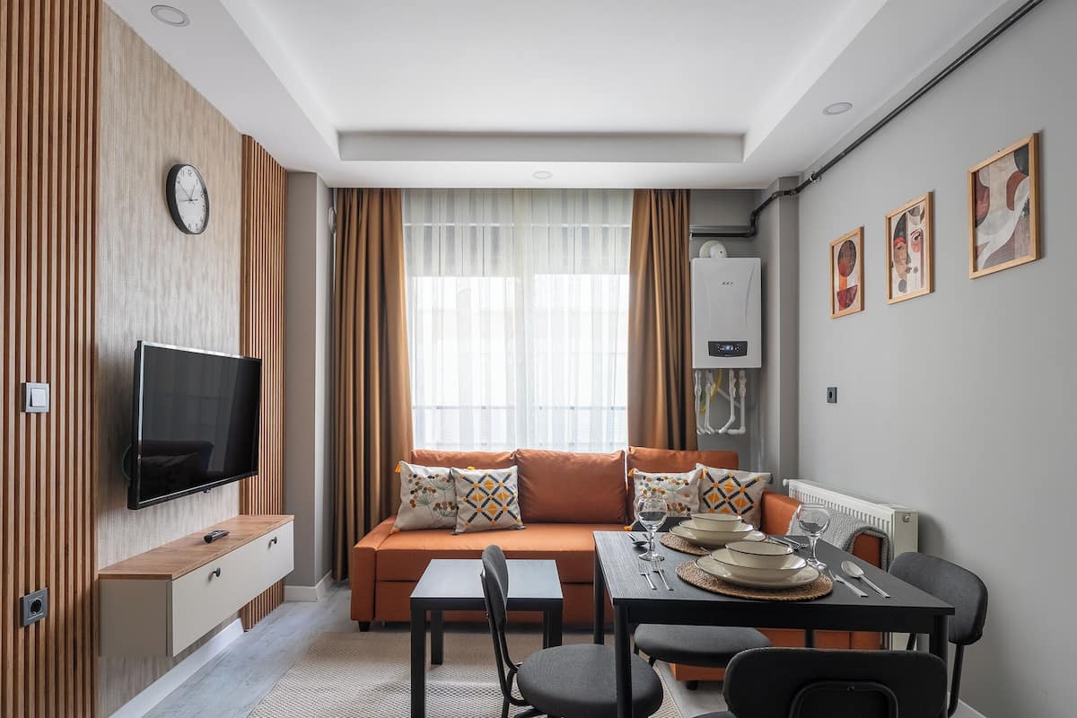 A modern living room with a sofa, TV, dining table, and artwork on the walls.