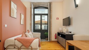 A modern living room with a sofa, a wooden table, a TV, and a door leading to an outdoor area. - Heat of the City: The Cozy Loft (Porto)