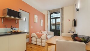 A compact living space with a kitchenette, a sofa, a dining table, and a view through a glass door. - Heat of the City: The Cozy Loft (Porto)