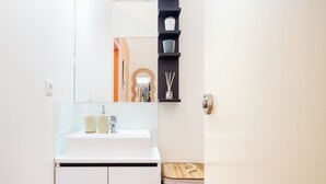 A modern bathroom with a white sink, mirror, and a wooden bench. - Heat of the City: The Cozy Loft (Porto)