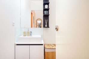 A modern bathroom with a white sink, mirror, and a wooden bench. - Heat of the City: The Cozy Loft (Porto)