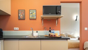 A kitchen with a microwave on a shelf, a sink, and a countertop with various items. - Heat of the City: The Cozy Loft (Porto)