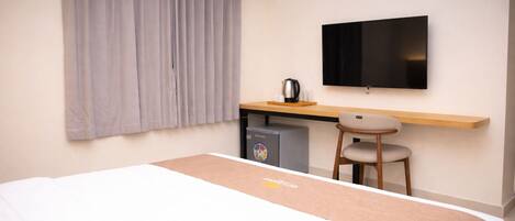 Een hotelkamer met een bed, bureau, stoel, televisie en een kleine koelkast.