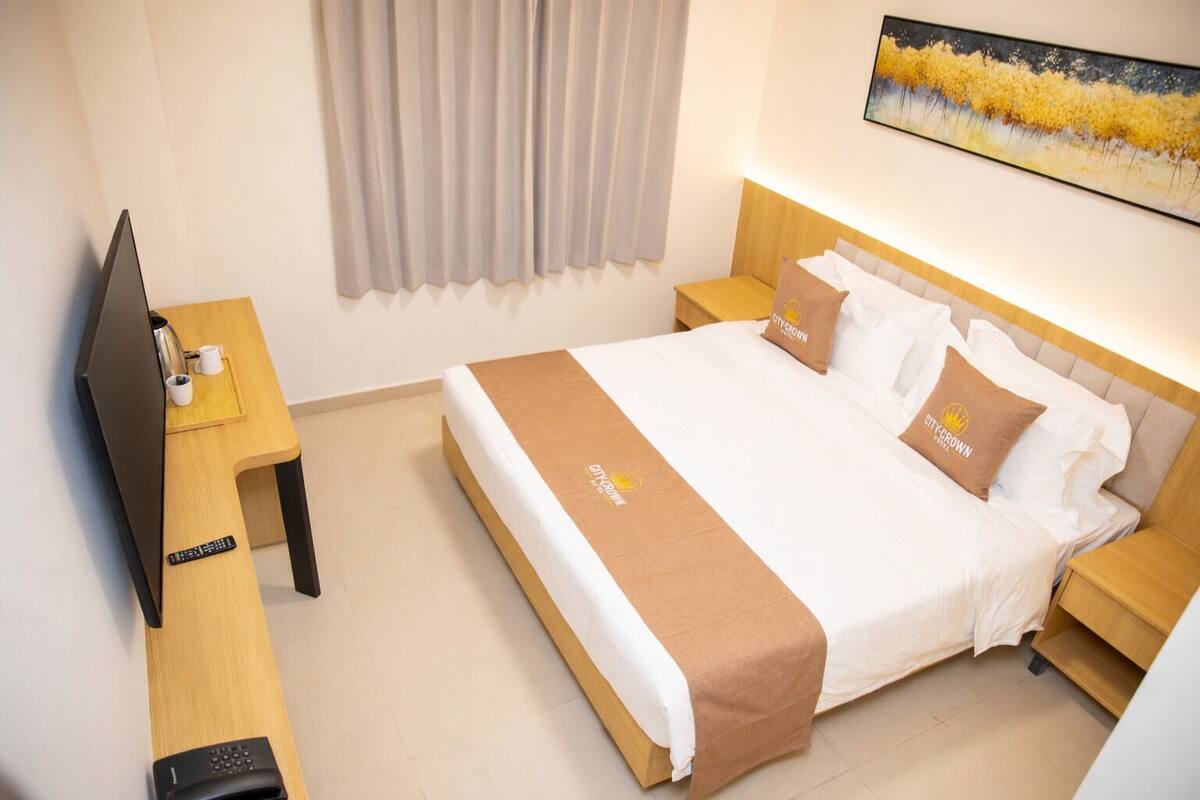 Una habitación de hotel con cama, televisión, mesita de noche y un cuadro en la pared.
