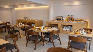 A breakfast area with wooden tables and chairs, a buffet counter with various food items, and a coffee machine. - City Crown Hotel (Dar es Salaam)