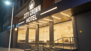 The exterior of the City Crown Hotel with a modern design, featuring a prominent crown logo above the name, large glass windows, and a staircase leading to the entrance. - City Crown Hotel (Dar es Salaam)