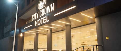 The exterior of the City Crown Hotel with a modern design, featuring a prominent crown logo above the name, large glass windows, and a staircase leading to the entrance.