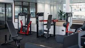 A modern gym with various exercise machines, large windows, and a view of the cityscape. - City Crown Hotel (Dar es Salaam)