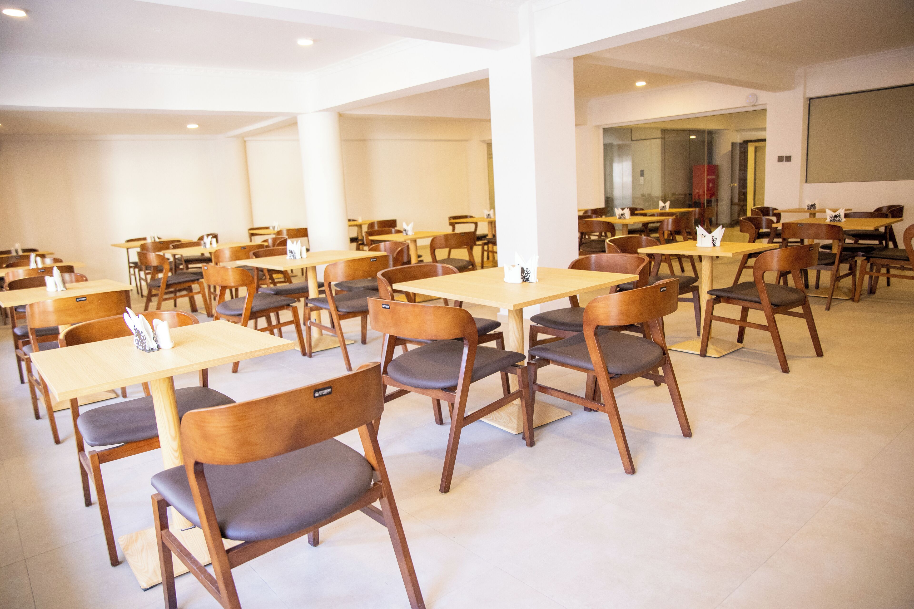 A spacious indoor dining area with multiple wooden tables and chairs, arranged in rows.