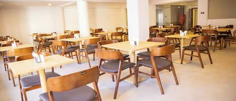 A spacious indoor dining area with multiple wooden tables and chairs, arranged in rows.