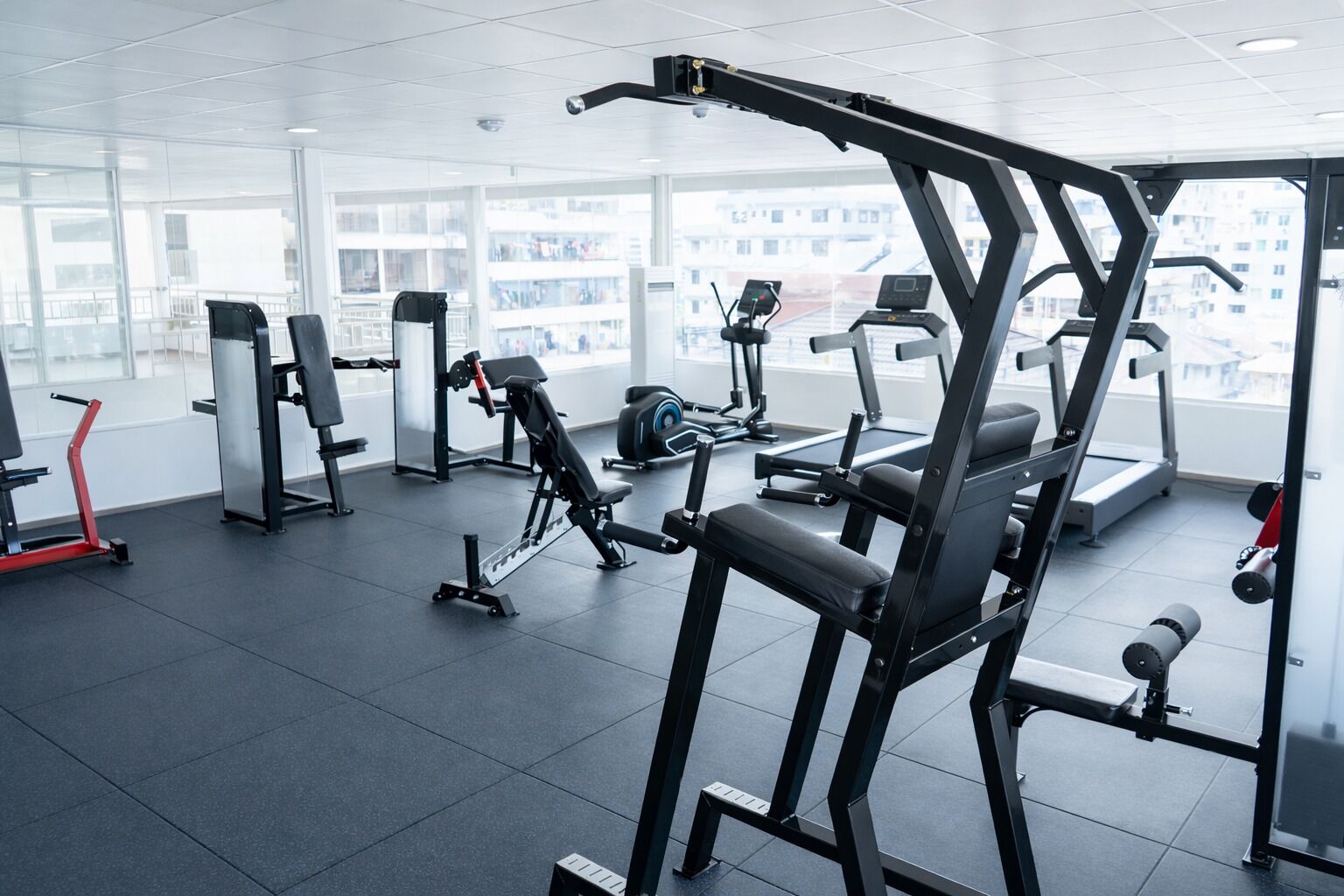 Une salle de sport moderne dotée de divers équipements d’entraînement, de grandes fenêtres et d’un aménagement propre et spacieux.
