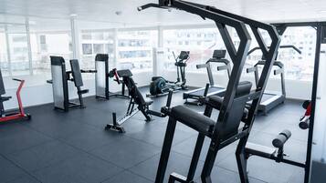 A modern gym with various exercise equipment, large windows, and a clean, spacious layout.