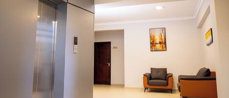 A modern lobby with a reception desk, two sofas, a painting, and an elevator.