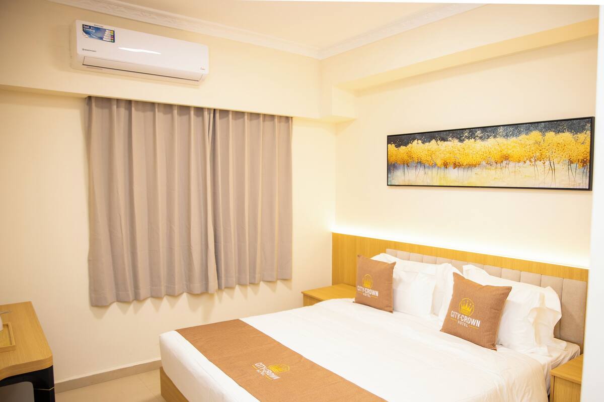Una habitación de hotel con cama, mesita de noche, aire acondicionado, un cuadro y cortinas.