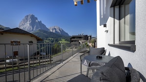 A terrace with outdoor seating, a mountain view, and a building with a white exterior. - 121A - Dosplain Panoramic Apartments | Odles (Santa Cristina Valgardena)