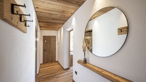 A hallway with wooden flooring, a wooden door, and a round mirror on the wall. - 121A - Dosplain Panoramic Apartments | Odles (Santa Cristina Valgardena)