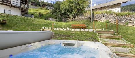 A hot tub in a garden with a wooden bench and stone wall.