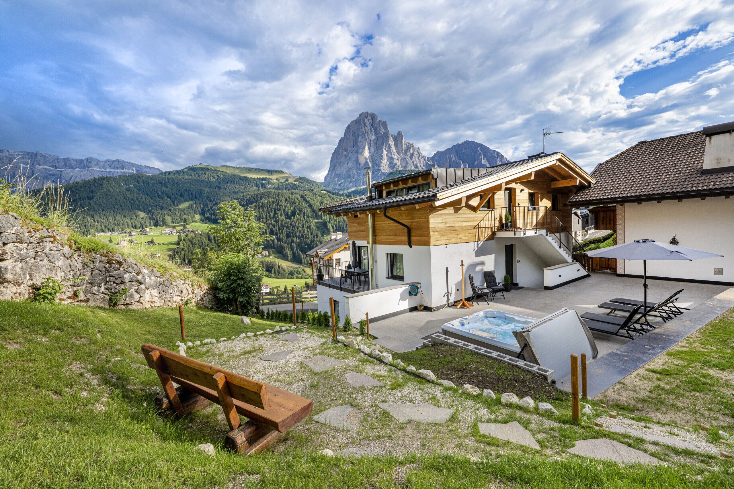 Un chalet moderne avec une façade en bois, un jacuzzi et une terrasse offrant une vue sur un paysage montagneux.