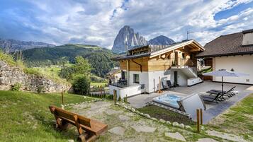 Un chalet moderne avec une façade en bois, un jacuzzi et une terrasse offrant une vue sur un paysage montagneux.