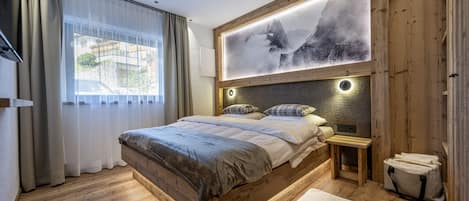 A modern bedroom with a wooden bed frame, a large window with curtains, a wall-mounted artwork, and a bedside table with a lamp.