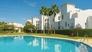 A swimming pool with a clear blue water surface, surrounded by a well-maintained lawn and palm trees. - Sun-Drenched Garden Apartment, Castillo Duquesa (Manilva)