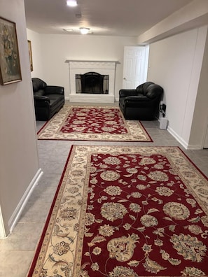 Ein Wohnzimmer mit zwei schwarzen Ledersofas, einem Kamin und zwei großen Teppichen in Rot- und Beigetönen.