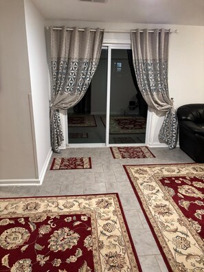 A room with a sliding glass door, a black leather sofa, and two patterned rugs on the floor. - Spacious Walkout Basement Suite Near National Harbor & DC (Fort Washington)