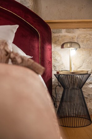 A bed with a red headboard, a bedside lamp, and a stone wall in the background. - Casa di Pietra Stone House (Kaštel Lukšić)