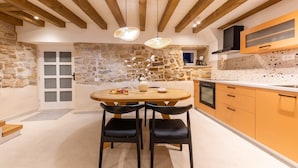 A modern kitchen with stone walls, wooden beams, and a round dining table with chairs. - Casa di Pietra Stone House (Kaštel Lukšić)