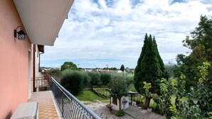 Un balcó amb vista a un jardí, un arbre alt i un paisatge llunyà.
