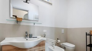 Un bany modern amb un gran mànec blanc, un vàter, una tassa i una prestatgeria de vidre sobre el mànec.