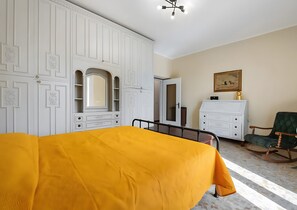 Un dormitorio con cama, armario, cómoda, silla y un cuadro en la pared.