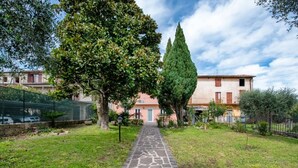 A stone pathway leading to a building with a garden and a tall tree. - Apartment 'Solarolo Cristina' with Lake View, Wi-Fi and Air Conditioning (Solarolo)